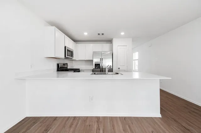 a view of kitchen with stainless steel appliances granite countertop a stove a sink a refrigerator and white cabinets with wooden floor