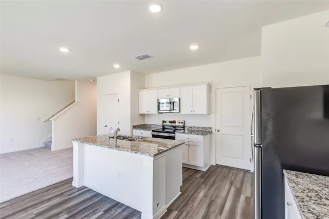 a kitchen with a sink a refrigerator a stove and white cabinets with wooden floor