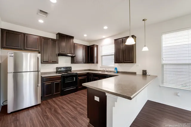 a kitchen with stainless steel appliances a sink dishwasher a refrigerator a stove top oven a kitchen island with wooden floor and cabinets