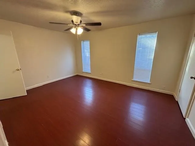 a view of an empty room with wooden floor and a ceiling fan