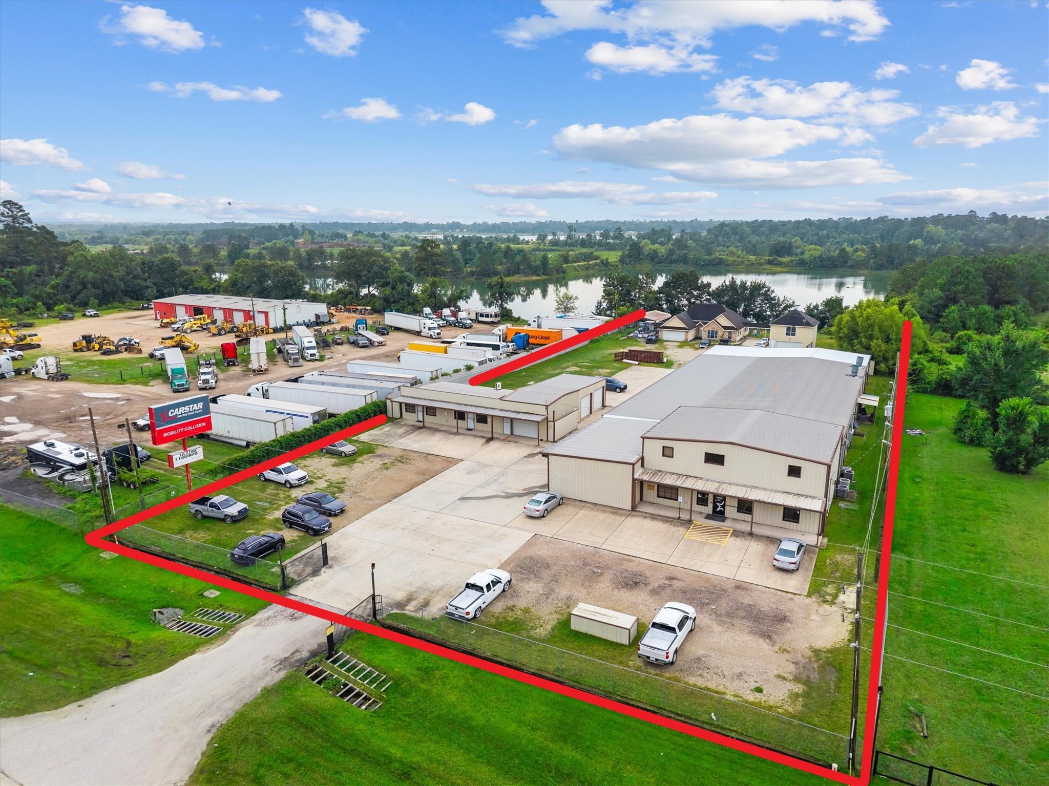 Commercial property with a large warehouse and ample parking, highlighted by a red boundary line. Situated near a scenic waterway and surrounded by greenery, offering easy access to main roads and nearby businesses.