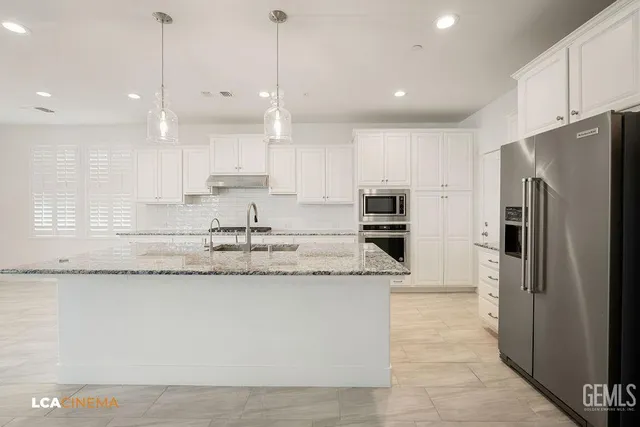 a large kitchen with stainless steel appliances kitchen island granite countertop a stove a sink a refrigerator and white cabinets with wooden floor