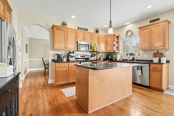 a kitchen with stainless steel appliances granite countertop a stove a sink dishwasher a refrigerator white cabinets and wooden floor next to a window