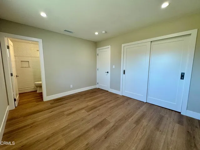 a view of an empty room with wooden floor and a bathroom