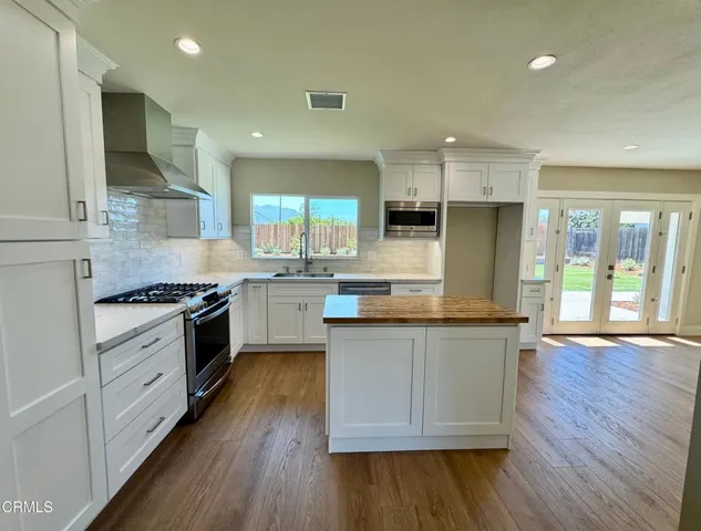 a kitchen with stainless steel appliances granite countertop a stove a sink dishwasher a refrigerator white cabinets and wooden floor next to a window