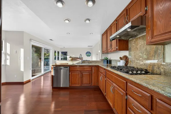 a kitchen with stainless steel appliances granite countertop a stove top oven a sink a dining table and chairs with wooden floor