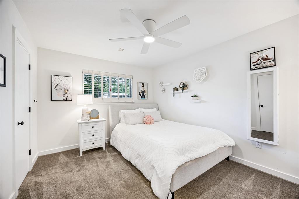 3151 Merrell Road Dallas, TX 75229 - Photo 18 of 25 Bedroom featuring a contemporary ceiling fan with integrated lighting, a window with plantation shutters, plush carpet flooring, a white nightstand with three drawers, and a built-in wall mirror