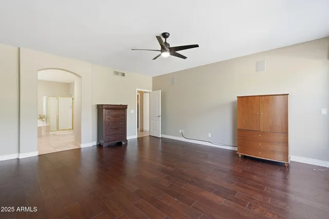 a view of an empty room with wooden floor and a ceiling fan