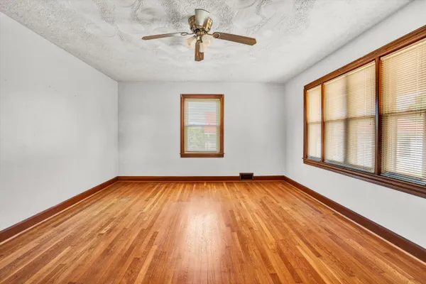 an empty room with wooden floor chandelier fan and windows
