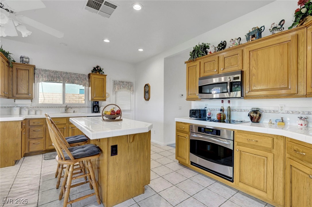 770 Fairway Drive Boulder City, NV 89005 - Photo 18 of 61 Kitchen with decorative backsplash, tile counters, appliances with stainless steel finishes, a kitchen breakfast bar, and light tile patterned floors