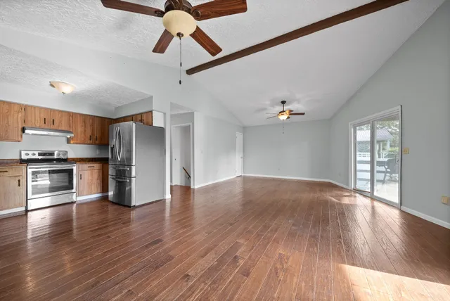 a view of an empty room with kitchen and window