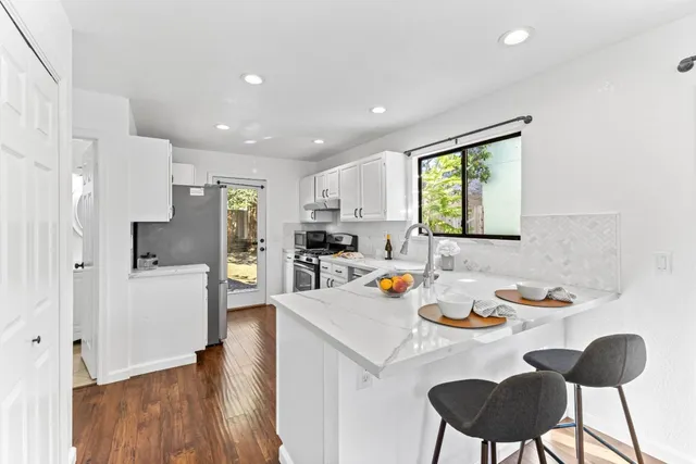 a kitchen with stainless steel appliances granite countertop a refrigerator a stove a sink a dining table and chairs with wooden floor