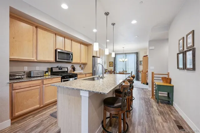 a kitchen with stainless steel appliances granite countertop a stove top oven a sink dishwasher a dining table and chairs with wooden floor