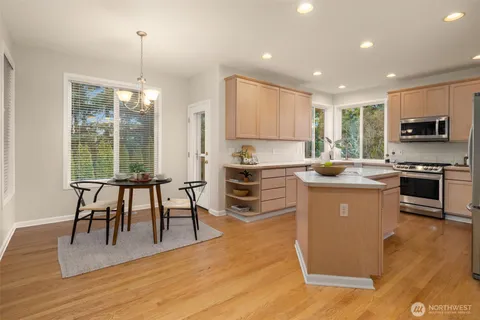 a kitchen with granite countertop a stove a sink a microwave a dining table and chairs with wooden floor