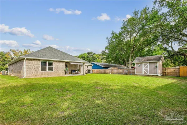 a house that is sitting in the grass with large trees and plants