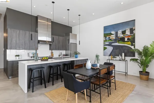 a room with stainless steel appliances kitchen island granite countertop a dining table chairs and a refrigerator