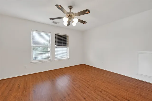 an empty room with wooden floor chandelier fan and windows