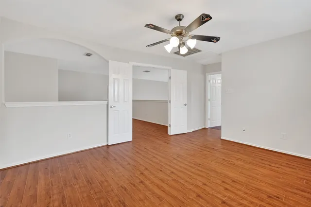 an empty room with wooden floor chandelier fan and windows