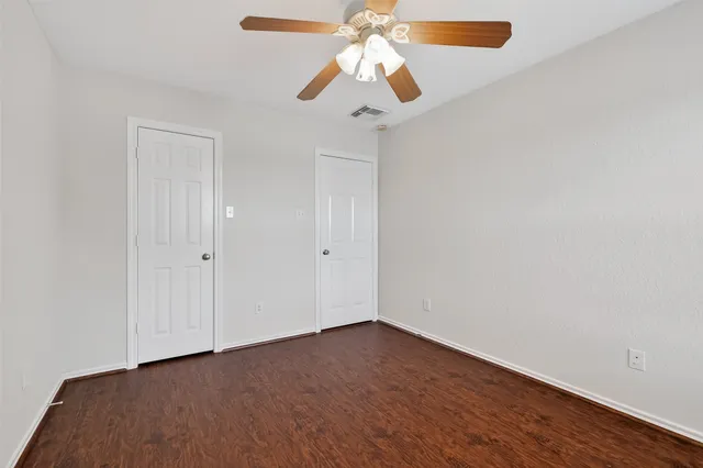 an empty room with wooden floor fan and windows