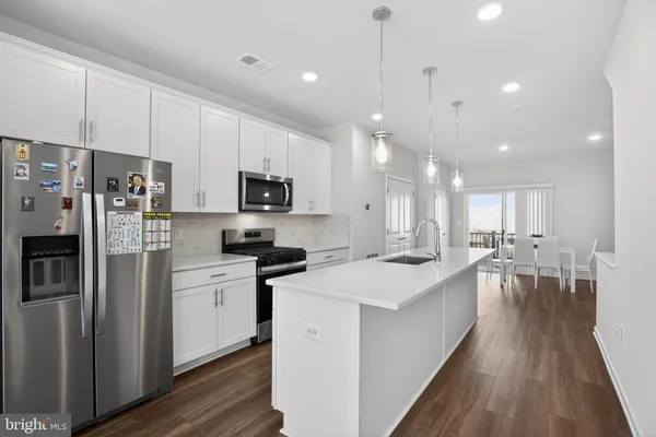 a kitchen with stainless steel appliances kitchen island granite countertop a refrigerator a stove a sink and white cabinets with wooden floor