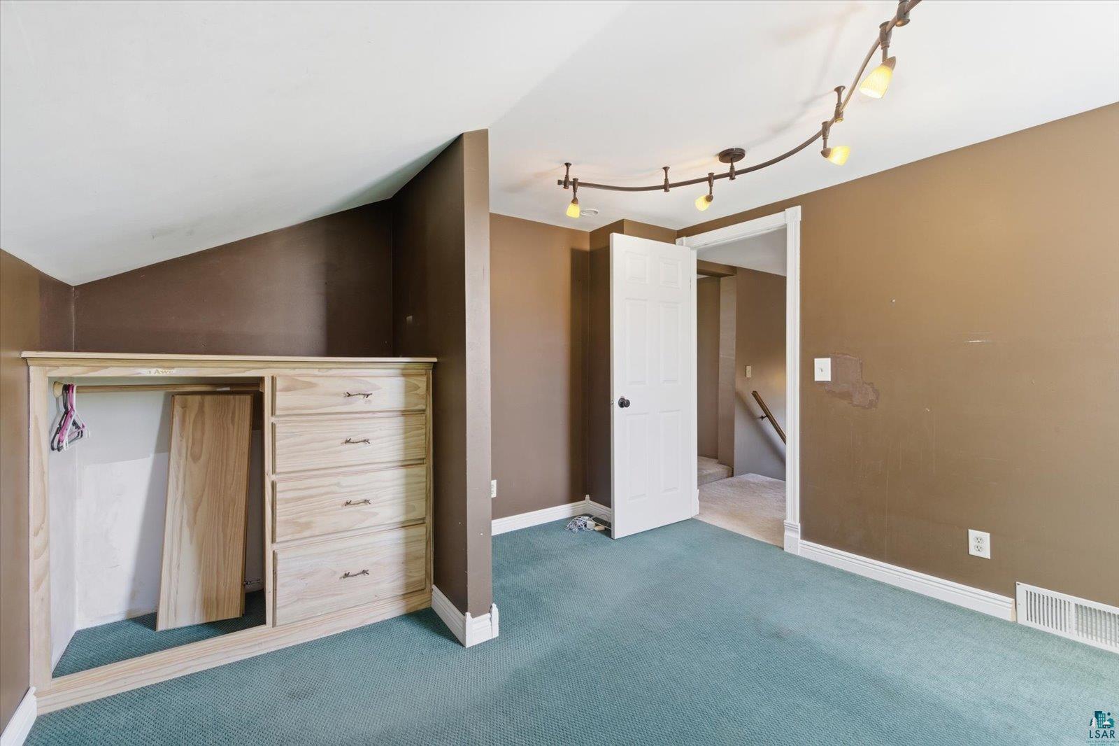 50 Main Street Soudan, MN 55782 - Photo 18 of 31 Angled ceiling room featuring track lighting, light wood-finish built-in dresser with four drawers, and light blue carpet flooring