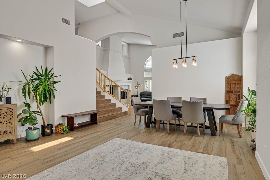 1259 Moon Vision Street Henderson, NV 89052 - Photo 4 of 53 Natural light illuminates a dining area with vaulted ceilings and wood flooring, connecting to a grand staircase.
