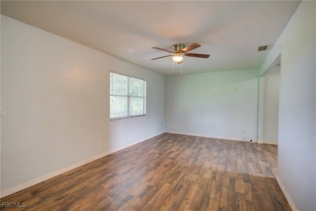 an empty room with wooden floor chandelier fan and windows