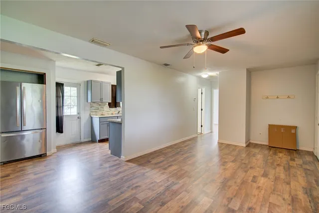 a view of an empty room and kitchen view with wooden floor