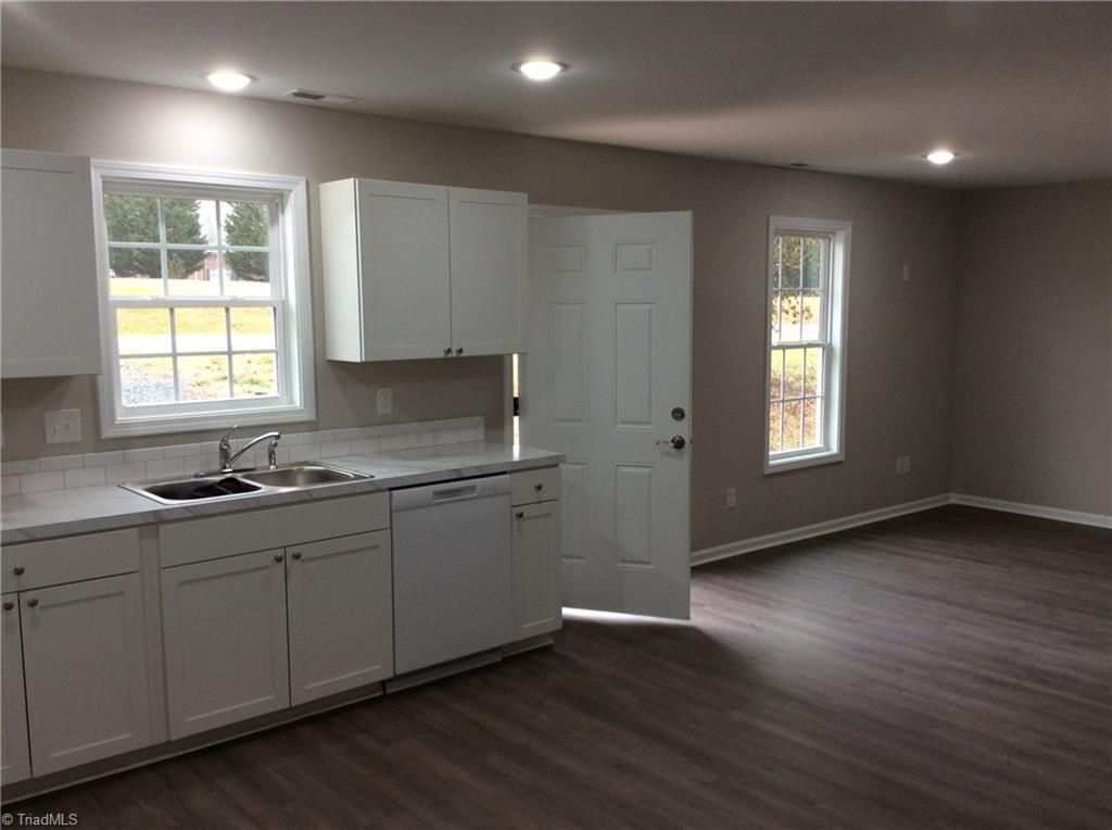 7739 Pine Street Rural Hall, NC 27045 - Photo 4 of 33 Kitchen: Features include vinyl plank flooring for easy cleaning, all new bright cabinets and counter tops, new fixtures, recessed lighting, fresh paint and a window over the sink so that you can see the outside world as you are cleaning up after that great dinner. The living room is over to the right side and the open door is the main entry door.
