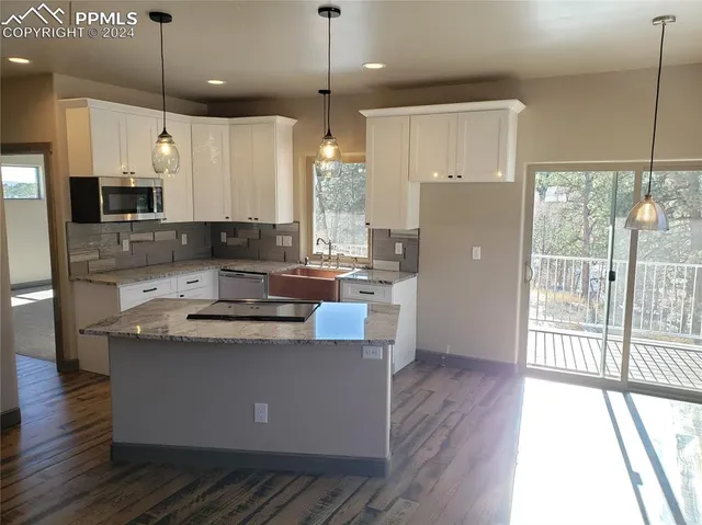 a kitchen with kitchen island granite countertop a refrigerator a oven a sink and white cabinets with wooden floor