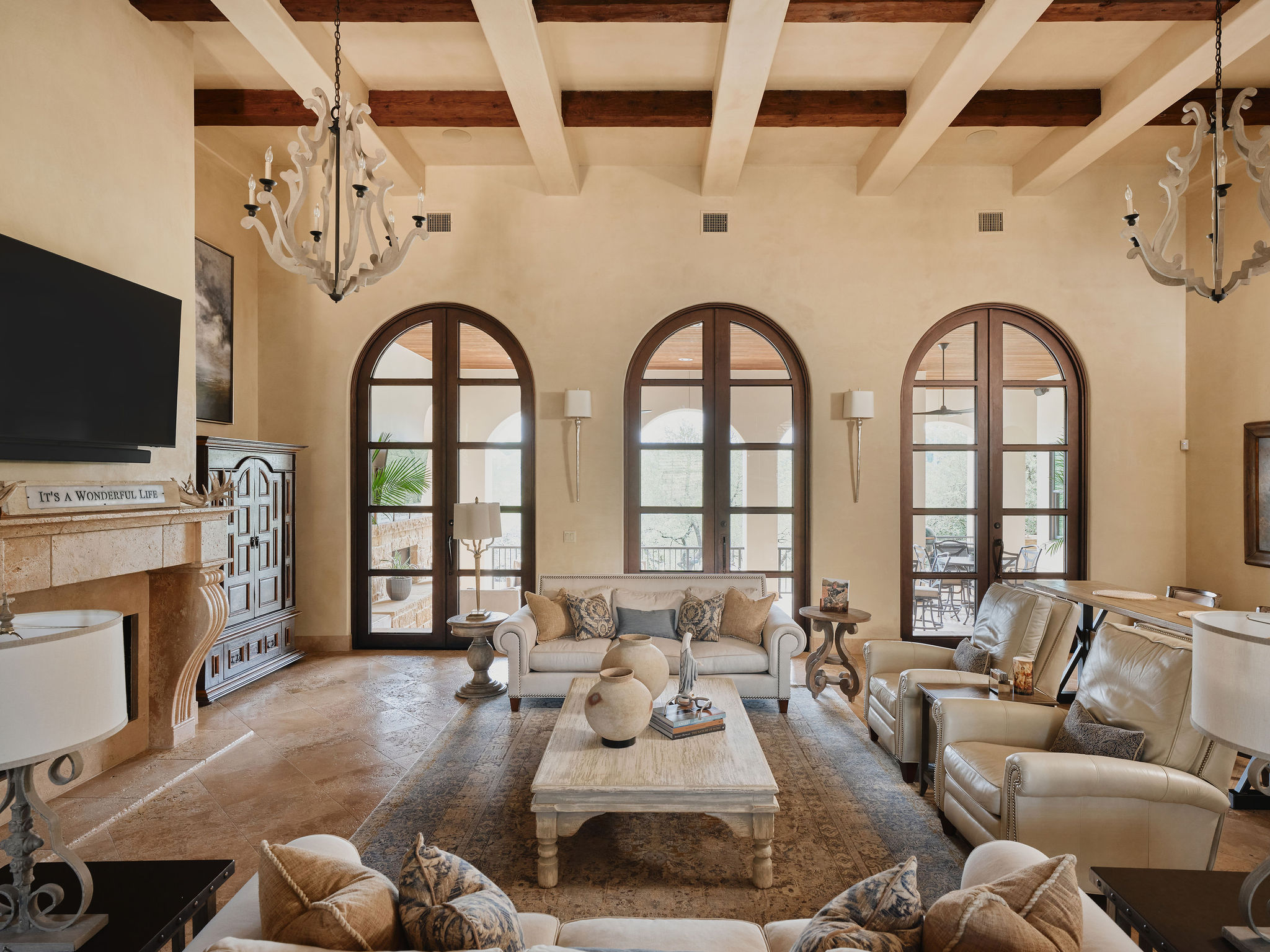 433 Brandon Way Austin, TX 78733 - Photo 6 of 40 Ornate chandeliers illuminate a grand living room featuring soaring beamed ceilings and graceful arched French doors.