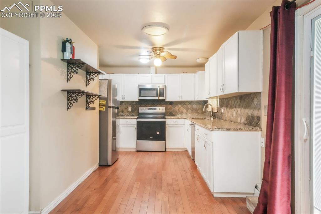 6802 Galley Road Colorado Springs, CO 80915 - Photo 9 of 50 a kitchen with stainless steel appliances a refrigerator a sink dishwasher a stove and white cabinets with wooden floor
