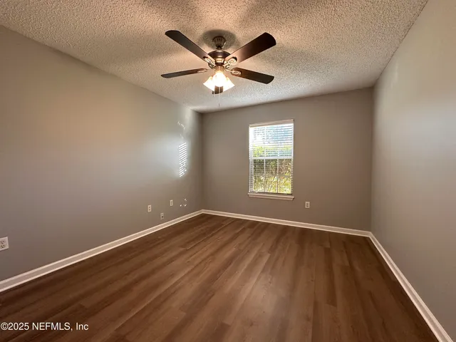 an empty room with wooden floor fan and windows