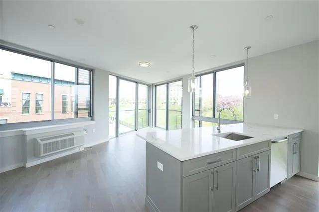 a hall with kitchen island a sink wooden floor and a large window