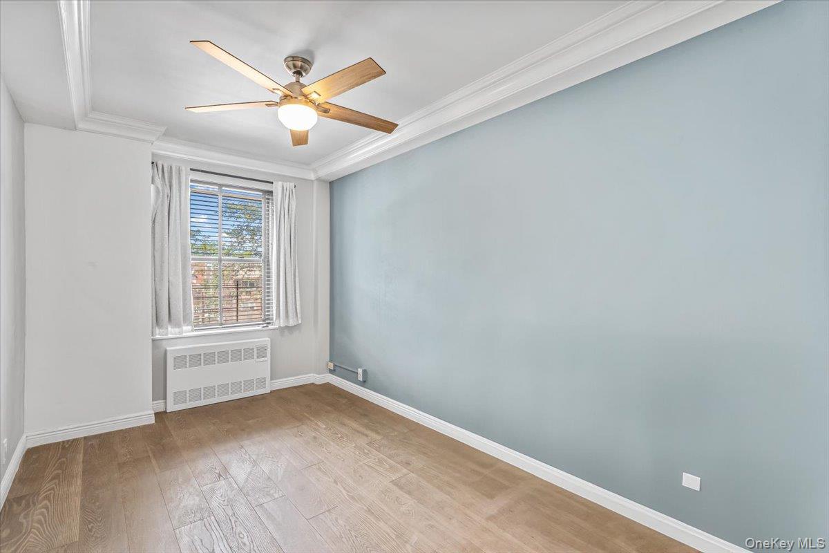 99-40 63rd Road, Unit 1Z Queens, NY 11374 - Photo 17 of 25 Spare room with radiator heating unit, crown molding, ceiling fan, baseboards, and wood finished floors