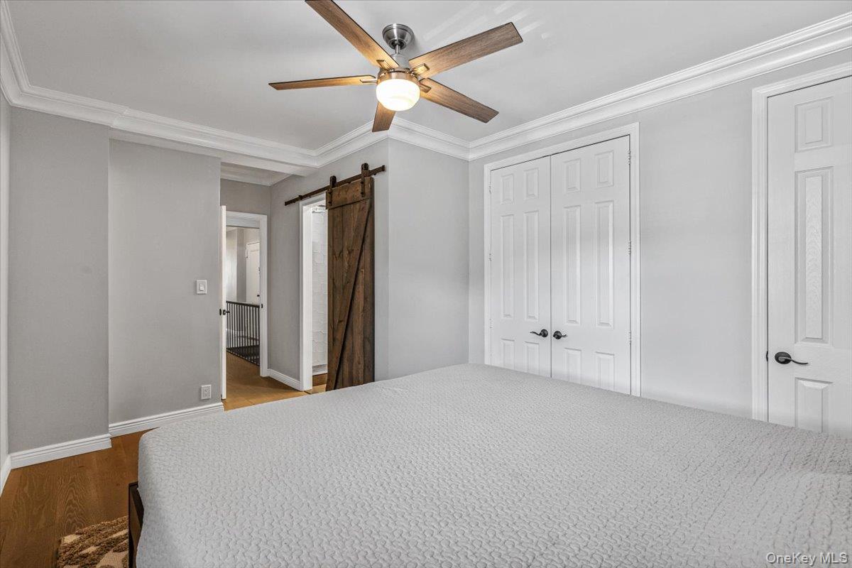 99-40 63rd Road, Unit 1Z Queens, NY 11374 - Photo 19 of 25 Unfurnished bedroom featuring a barn door, ornamental molding, a closet, wood finished floors, and baseboards