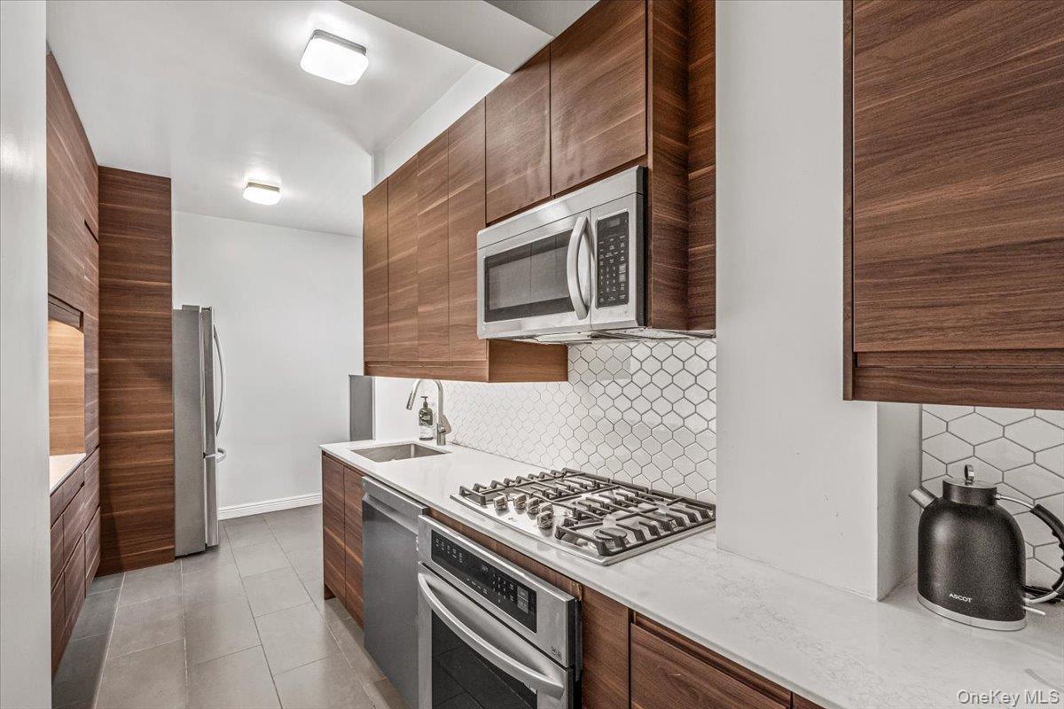 99-40 63rd Road, Unit 1Z Queens, NY 11374 - Photo 9 of 25 Kitchen with stainless steel appliances, a sink, decorative backsplash, modern cabinets, and light countertops