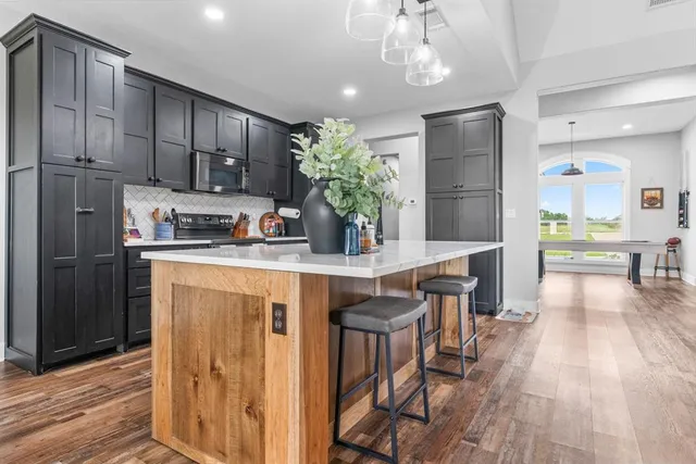 a kitchen with stainless steel appliances granite countertop a refrigerator a sink dishwasher a stove and a dining table with wooden floor