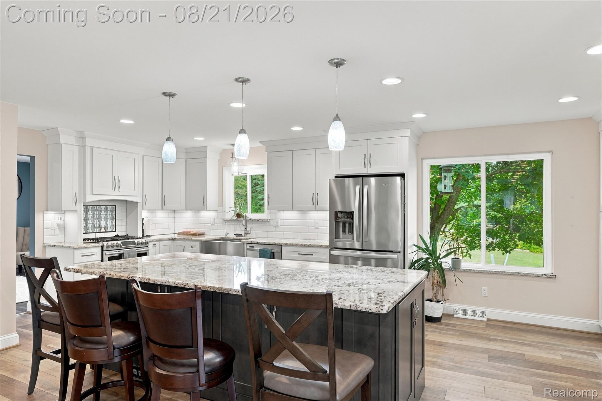 6060 Ford Road Commerce Township, MI 48382 - Photo 15 of 58 Spacious kitchen featuring an expansive center island with seating, stainless steel appliances, white shaker cabinetry, and wood-finish flooring