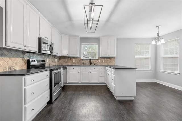 a kitchen with stainless steel appliances granite countertop a stove a sink dishwasher and white cabinets with wooden floor