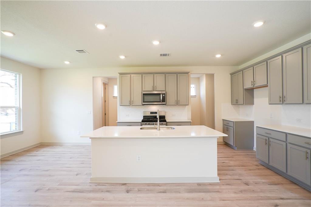 2341 Gabriels Horn Road Leander, TX 78641 - Photo 4 of 20 Kitchen featuring light wood-style flooring, an island with sink, recessed lighting, stainless steel appliances, and gray cabinetry