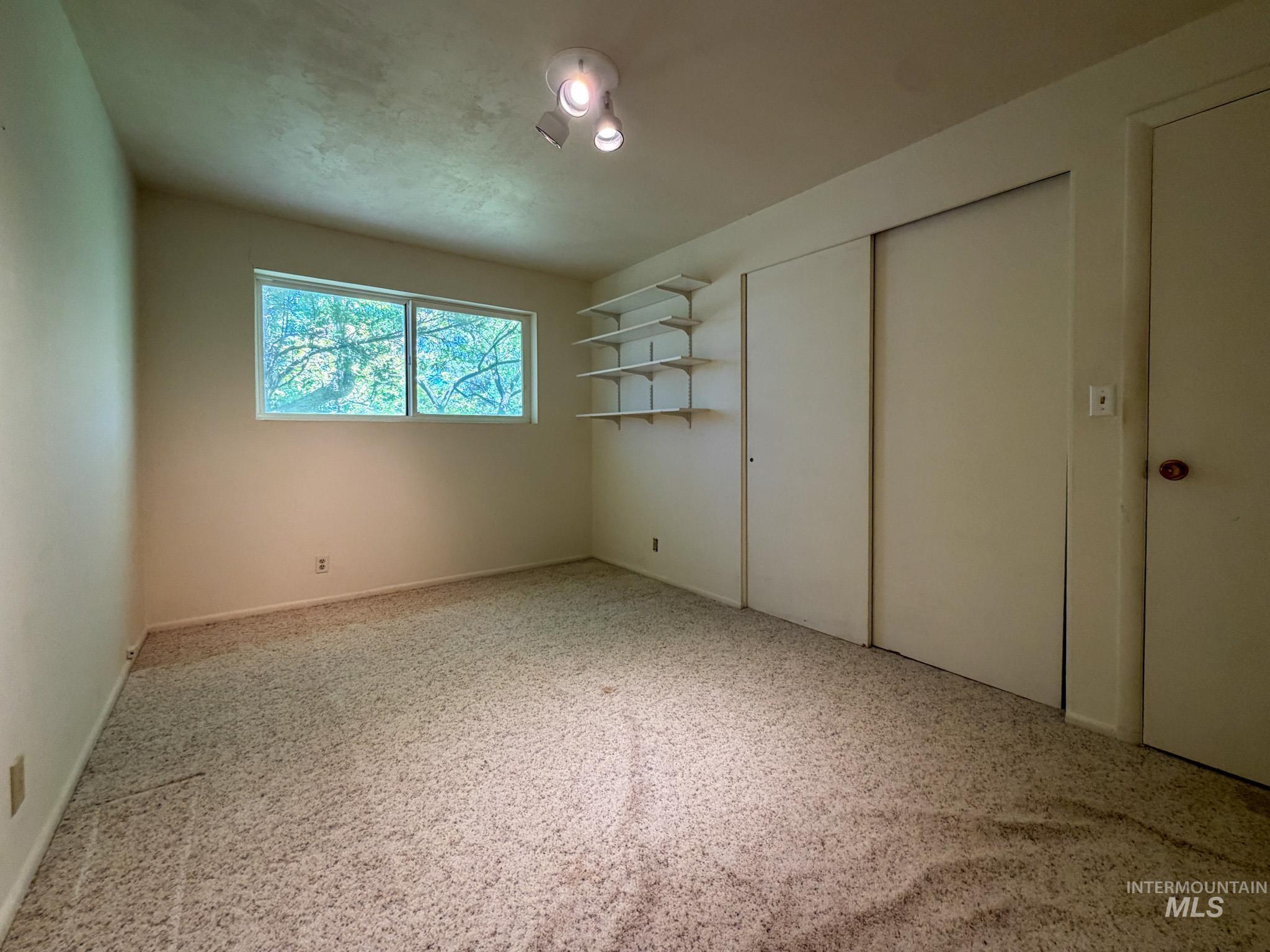 1924 H Street Rupert, ID 83350 - Photo 10 of 13 Room featuring light-toned carpeting, a window with outdoor tree scenery, integrated shelving, and sliding closet doors
