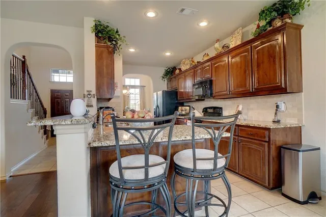 a kitchen with stainless steel appliances granite countertop a sink a stove a refrigerator cabinets and chairs