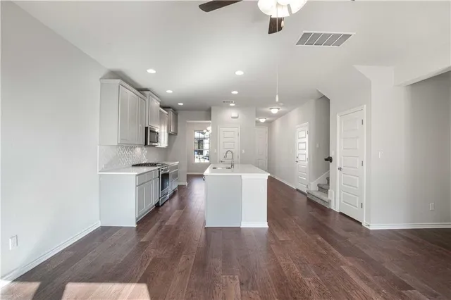 a living room with stainless steel appliances kitchen island hardwood floor and a sink