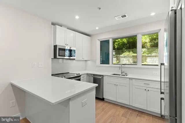 a kitchen that has a sink a microwave oven a stove and white cabinets with wooden floor