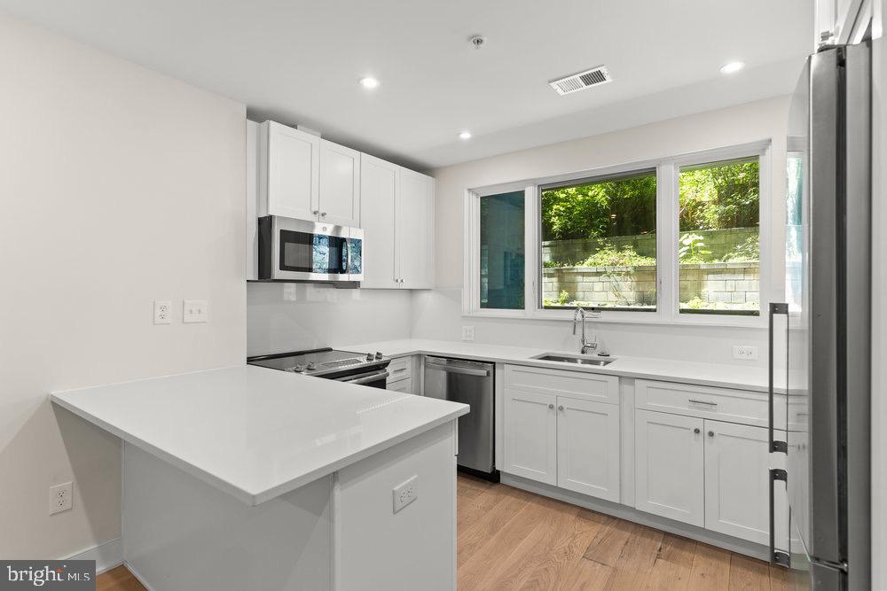 3016 Dumbarton Street Northwest, Unit 102 Washington, DC 20007 - Photo 17 of 23 a kitchen that has a sink a microwave oven a stove and white cabinets with wooden floor