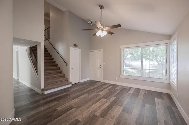 a view of an empty room with wooden floor ceiling fan and window
