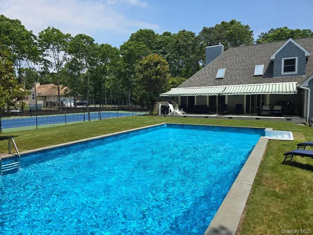 a view of swimming pool with lawn chairs and large trees
