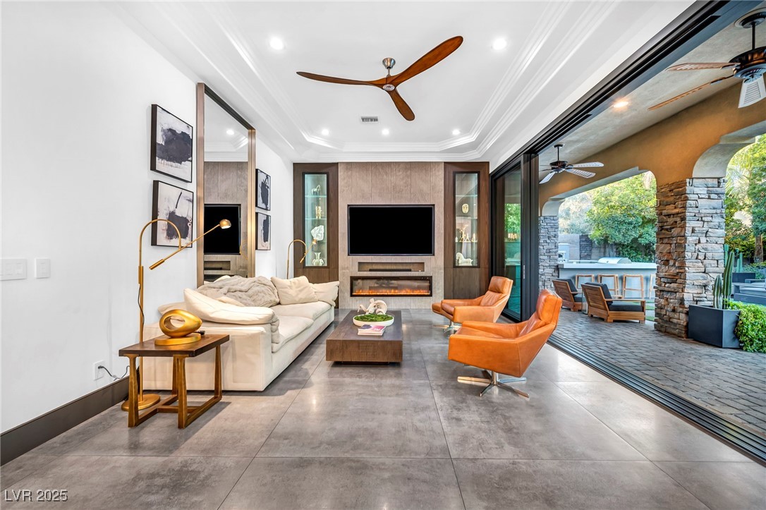 8032 Spring Buck Court Las Vegas, NV 89129 - Photo 14 of 41 Living room featuring a glass covered fireplace, italian porcelain tiles, crown molding, a tray ceiling, and recessed lighting