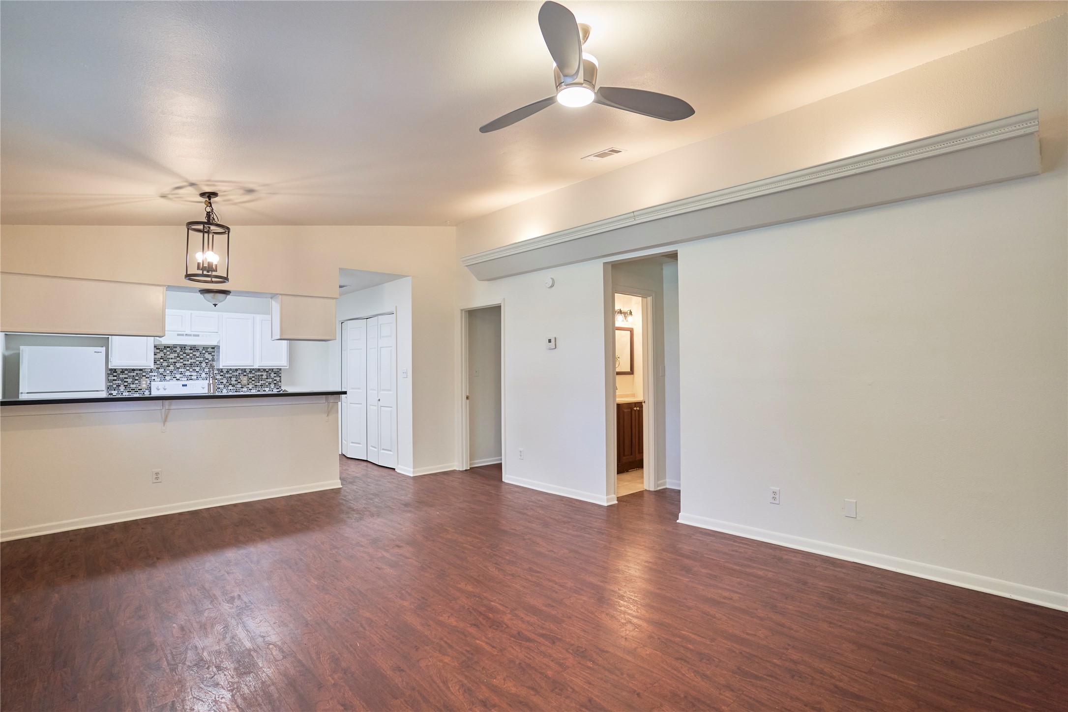 23393 Nameless Road, Unit 171 Leander, TX 78641 - Photo 3 of 15 An open-concept living area features rich wood flooring, a pass-through to the kitchen, and a ceiling fan.